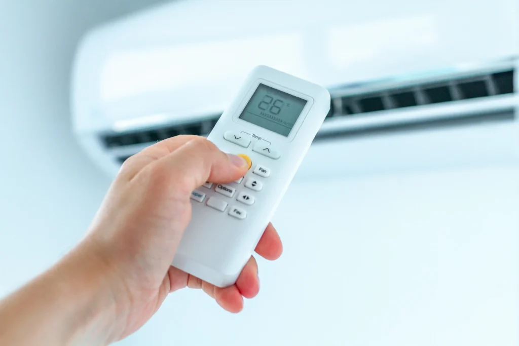 Main tenant une télécommande réglant une climatisation à 28 degrés dans une pièce lumineuse